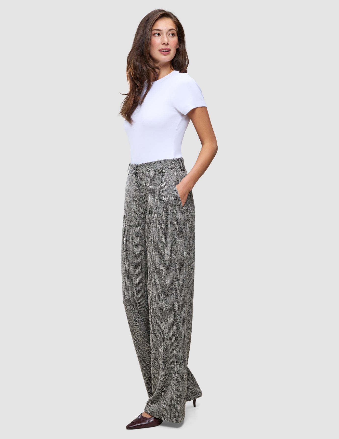 Eine Frau, die ein weißes T-Shirt und die Women Ashryn Pants Wide Domino Herringbone trägt, eine graue, gemusterte Bouclé-Hose mit weitem Bein und Vordertaschen.